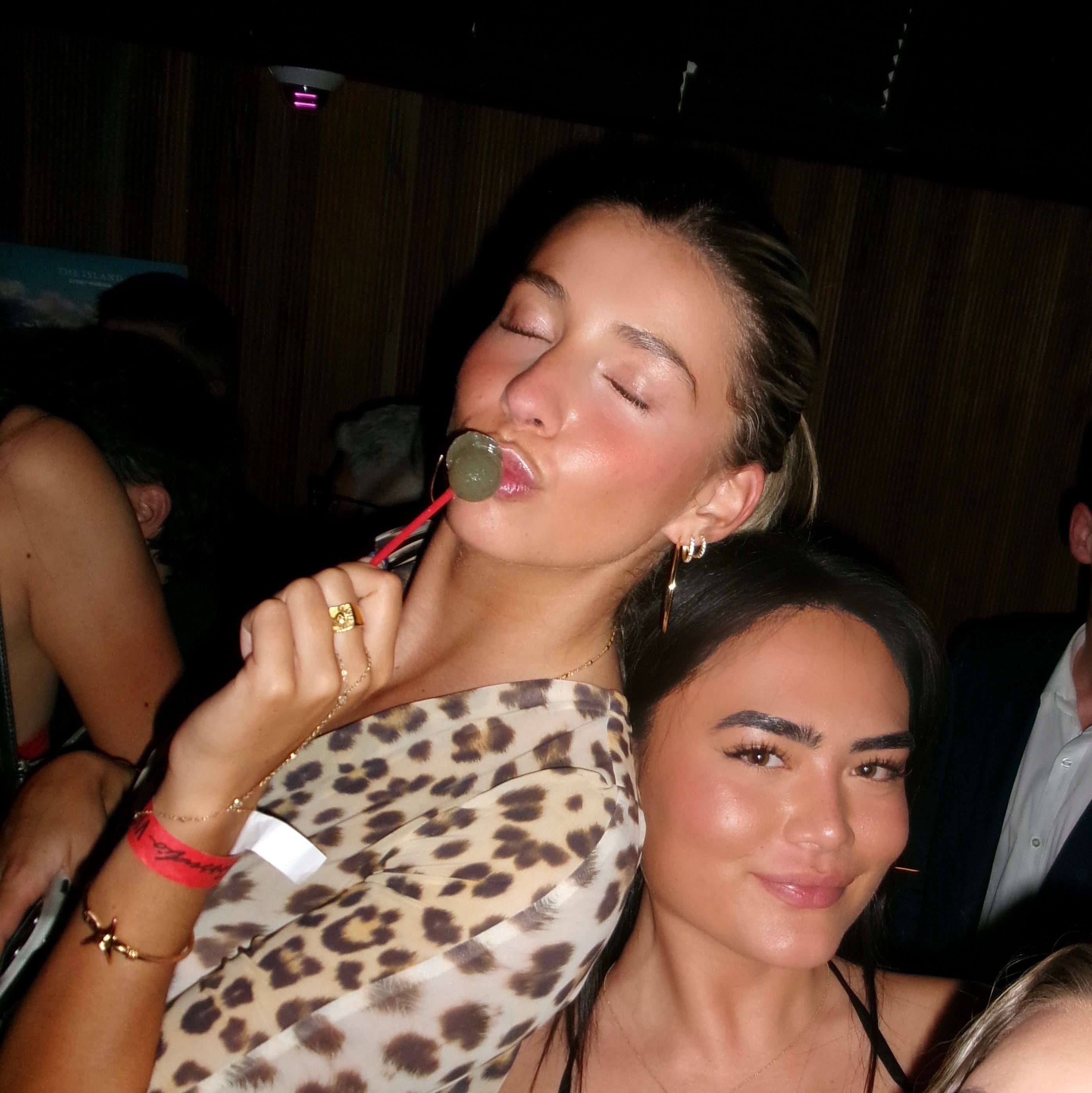 Two women at a social event, one with a lollipop